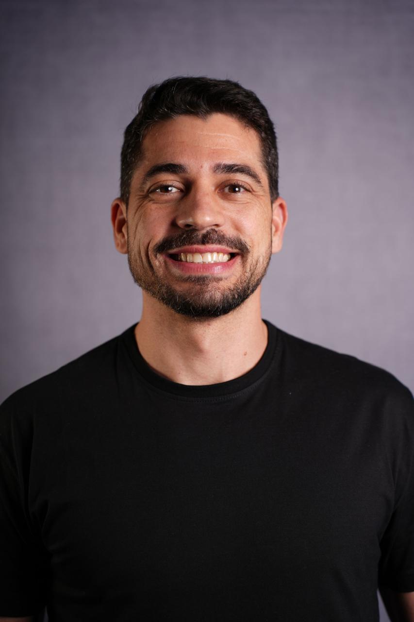 Adriano Basili sorrindo, usando camiseta preta, em retrato profissional